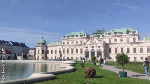 People walk on a path in front of Belvedere Castle in Austria on a sunny day