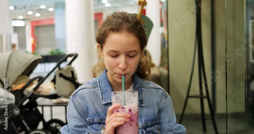 Young focused girl sips pink refreshment drink while eyes close in enjoyment. Refreshing taste meets quiet atmosphere creating peaceful break