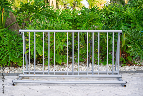 A silver bike rack stands ready on smooth stone pavers, framed by a lush wall of vibrant green vegetation in the background.