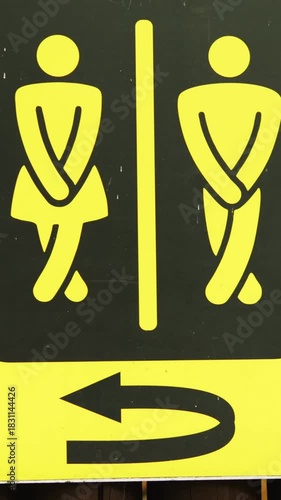 Drawn yellow and black sign indicates public restrooms for men and women with curved arrow suggesting direction. Picture on wooden fence in outdoor public space vertical video