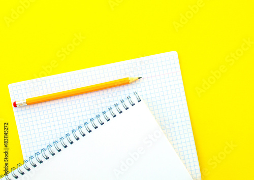 White notebook with spring, checkered notebook and pencil.