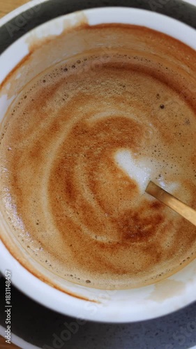 Foamy creamy latte unfinished cup with golden teaspoon and porcelain saucer on wooden counter. Drinking fresh coffee with foam from ceramic mug in cafe vertical video