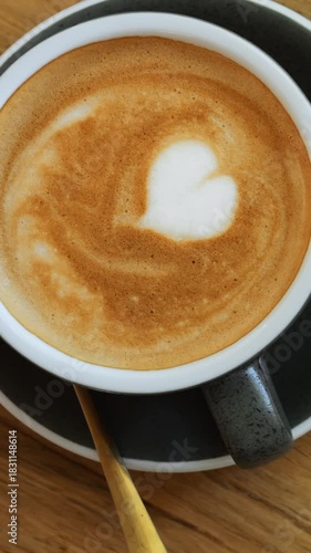 Cappuccino with cream heart pattern dressing and tasty small cake on wooden table. Lunch with luxury dessert and sweet hot drink in porcelain cup served in cozy cafe vertical video