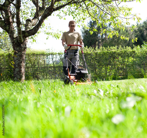 Young Man Mowing Lawn in Spring Garden