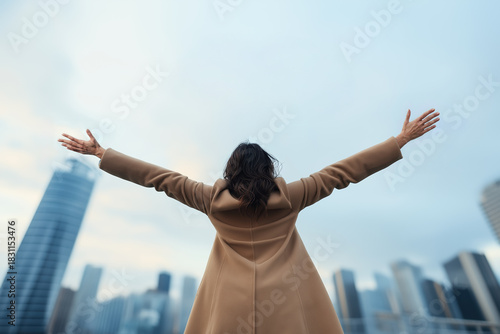 Woman spreading arms wide, embracing success and achievement, standing with an urban cityscape and clear sky in the background, symbolizing hope, business growth, and future opportunities