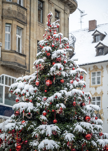 A pretty Christmas tree decorated with red baubles at the market place is covered in snow. Constance, Baden Württemberg, Germany.