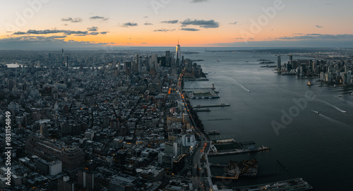 Aerial view of a sprawling cityscape where the Hudson River reflects the warm glow of the setting sun, illuminating the iconic One World Trade Center, New York, New York, United States.