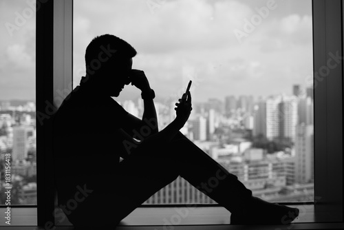 silhouette man stressed while looking at phone by window