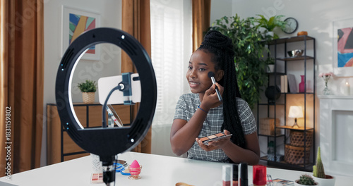 Influencer creates beauty content at home, teaching followers how to use bronzer and highlighter. She carefully defines her cheekbones and blends products into her skin.