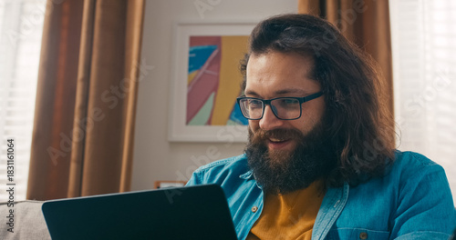 A man uses his laptop when his friend calls through video chat. He greets them with a wave and talks openly about shared topics.