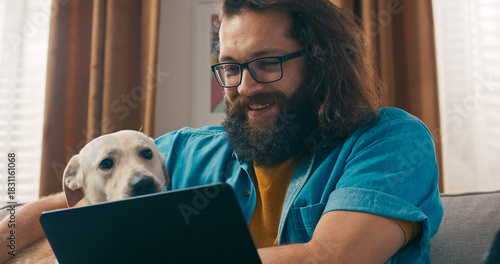 A happy remote worker pauses from his laptop duties to chat with a friend on a video call, waving and smiling warmly.
