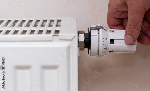 Hand adjusting the thermostat of a white radiator to control heating in a home. This action is key for energy efficiency during colder months.