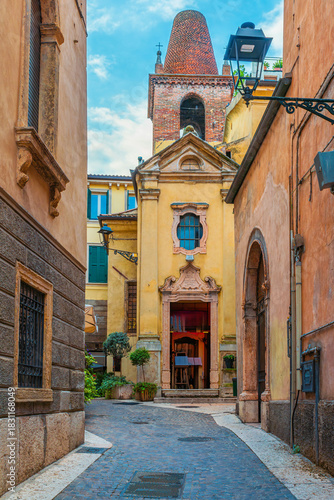 Medieval narrow street in Verona old town with colorful building facades and yellow facade of church with brick bell tower under blue sky Veneto, Italy. Italian architecture. Vertical orientation