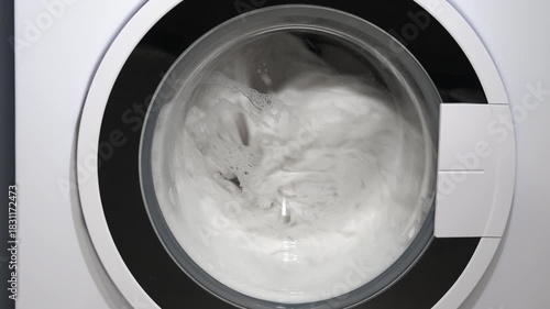 Washing machine drum rotating with laundry and soap. Front-loading washing machine spinning clean white clothes with soap and water during a wash cycle, representing modern household chores