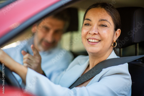 Happy woman driving car with male passenger pointing and smiling