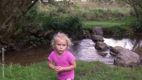 Two little girls exploring nature by a stream in the countryside on a summer afternoon