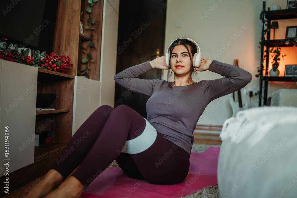 Fototapeta premium Woman exercising sit-ups with resistance band at home