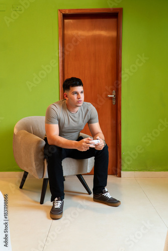 Young man playing videogames, sitting on the couch while using a joystick