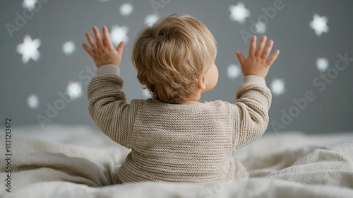 Caucasian toddler reaching for glowing stars on bedroom ceiling