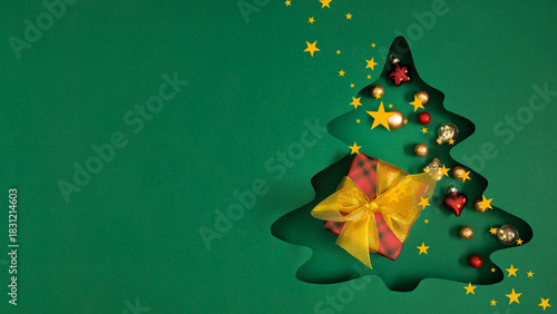 Elegant minimalist green Christmas background with a cut-out silhouette of a Christmas tree with a gift wrapped in red and black checkered paper and decorated with a lush golden bow. Christmas decor