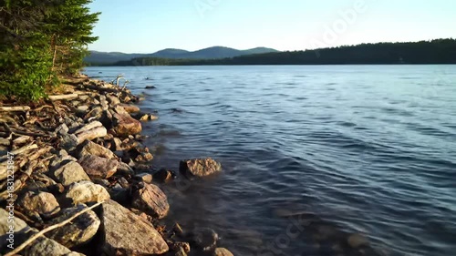 Peaceful lakeside shoreline with gentle water waves and forested horizon