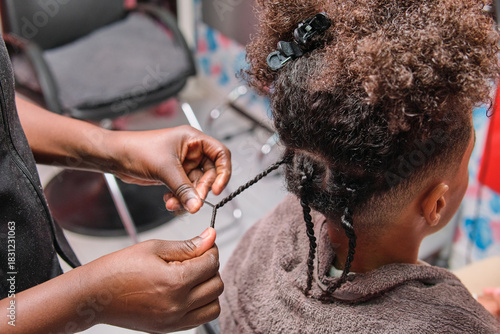 Afro young man getting African braids styled by hairstylist from rear view