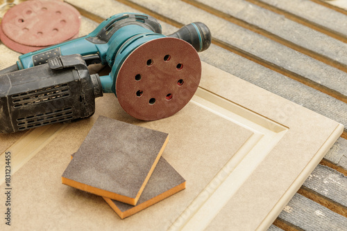 Orbital sander and sanding pads on cabinet door panel in carpentry workshop