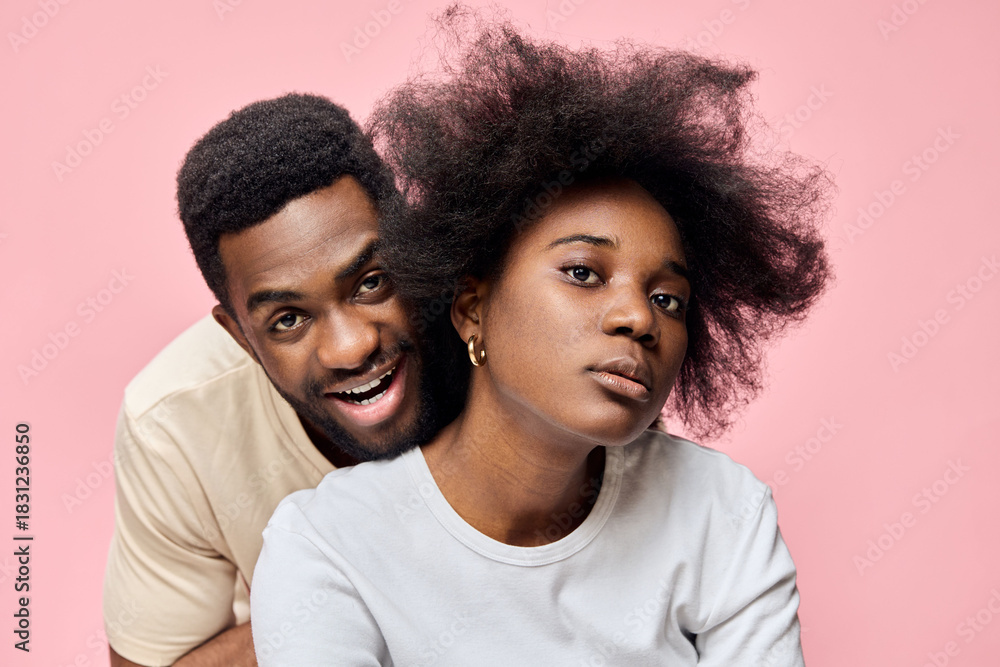 Obraz premium A joyful couple poses together in front of a pink background, showcasing natural hairstyles, vibrant emotions, and modern fashion choices, reflecting love and happiness