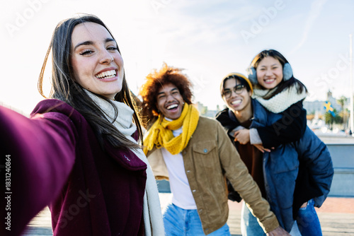 Diverse group of young people having fun taking selfie portrait together outside during winter season