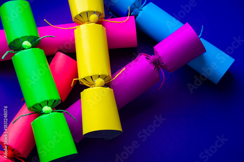 Brightly colored Christmas crackers piled onto a background of purple copy space