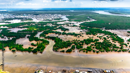 Aerial view of winding waterways carving through lush green vegetation, meeting the muddy river as settlements dot the landscape, Port Harcourt, Rivers, Nigeria.