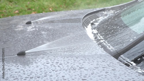 close-up view shows car windshield wipers actively cleaning the glass as fluid is sprayed. The clear sound of the washer jets