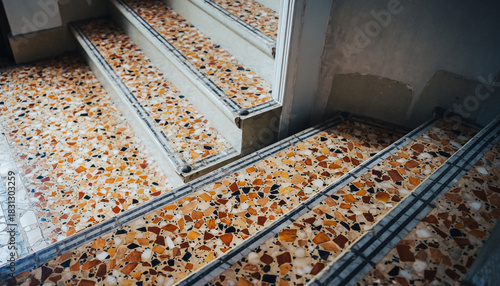 Ornate terrazzo stairs ascend with mosaic tile borders and a worn concrete wall