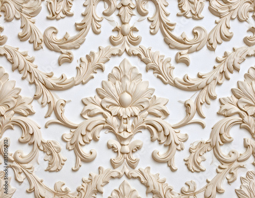 Detailed beige classical floral and scroll plasterwork on a white wall. An elegant, ornate background with intricate decorative molding.