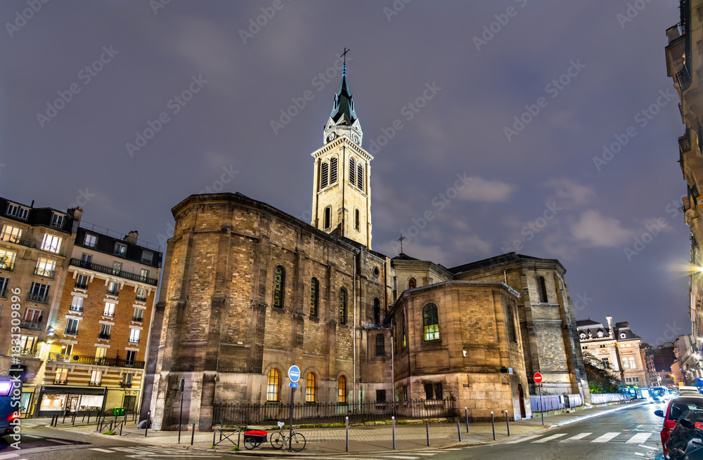 Fototapeta premium Church of Notre-Dame of Clignancourt in Paris, France. Historic Neo-Romanesque building stands on Place Jules Joffrin under a cloudy night sky