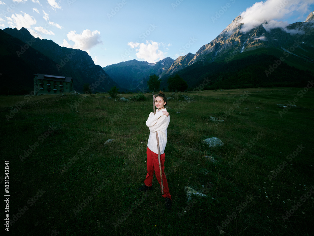 Fototapeta premium Child, girl, mountain valley landscape with open field and rugged peaks, wearing white jacket and red pants, standing confidently in a wide alpine setting for outdoor adventure