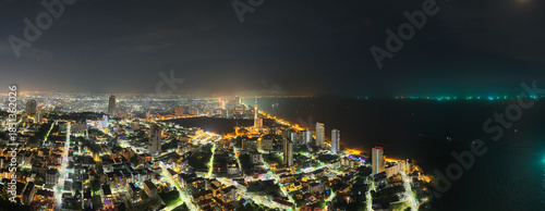 Panoramic aerial view of Pattaya at night, glowing urban skyline along the coastline and shimmering lights reflecting over the dark sea.