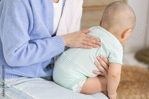 Tableau sur toile Close-up of Asian mother gently burping her baby after feeding, showing care and post meal routine