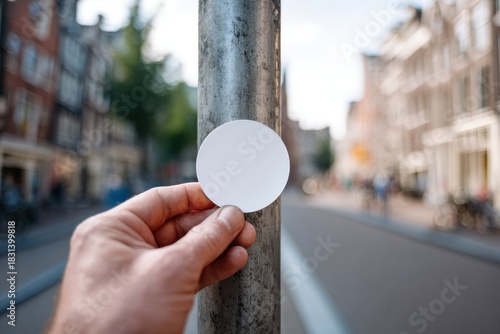 Hand holding blank white sticker against blurred european city street background