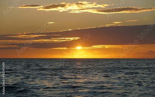Sunset over ocean creates warm light reflections and layered clouds, signaling end of day and stable weather conditions near Madeira Beach, Florida, U.S.A