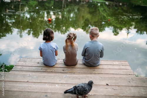 Children sitting by a tranquil lake on a sunny day