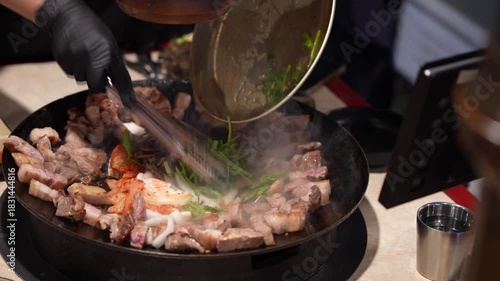 Authentic Korean Food Experience, Adding Kimchi and Vegetables to Sizzling Pork Belly on Korean BBQ Griddle, Cooking Pork and Spicy Kimchi Together on Hot Plate