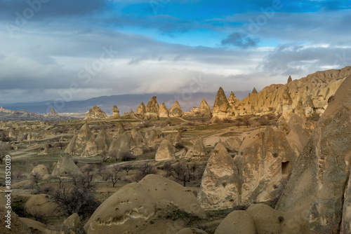 Landscape of unique fairy chimneys and rocky hills in Cappadocia, Turkey, under a dramatic blue and gray sky.