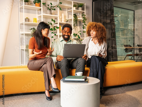 Diverse Team Collaborating On Laptop In Modern Office Lounge Set