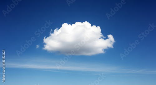 A single cumulus cloud floating in a bright blue sky with light wispy clouds below it in the distance