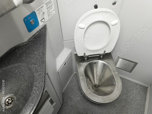 Public restroom in a commuter train car. A metal toilet, white walls, and a gray sink