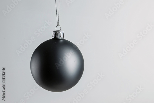 Minimalist single black matte Christmas ball hanging on string against white background.