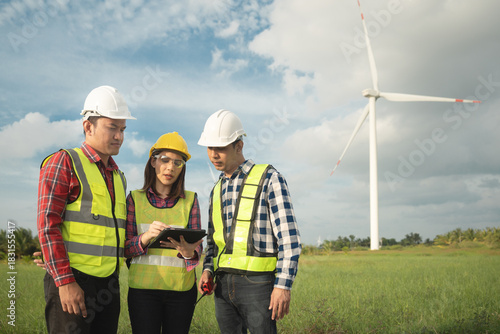 Renewable energy maintenance. Engineer using digital tablet checking system of wind turbine at windmill field farm station. Wind turbine energy storage system. Workers meeting to check around the area