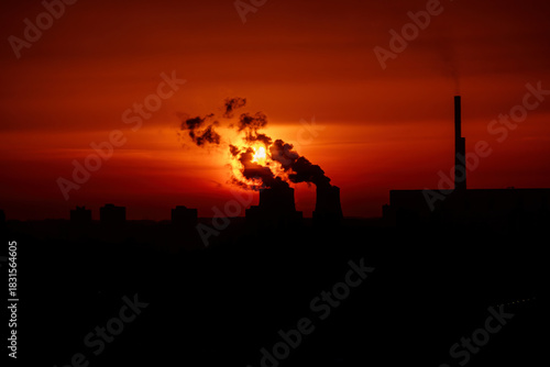 A silhouette of a power plant against a fiery sunset, creating a stark contrast between the natural beauty and industrial landscape