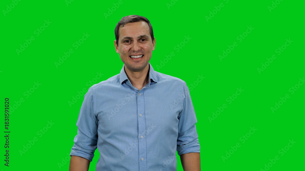 Fototapeta premium Portrait of young smiling man in light blue colored shirt standing against green background